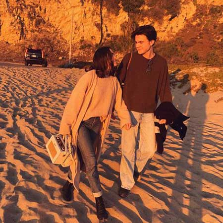 Bailee Madison y Blake Richardson caminando sobre la arena durante la noche
